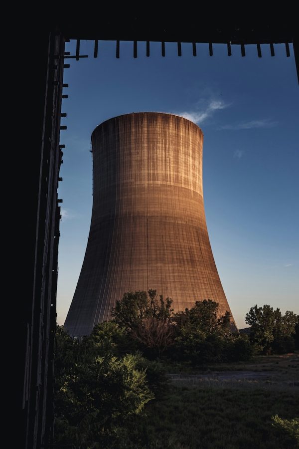 A nuclear reactor cooling tower stands over a green tree landscape.